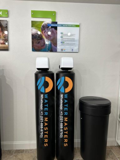 Two tall black water filtration tanks with "Water Masters" logos, next to a trash bin and photos.